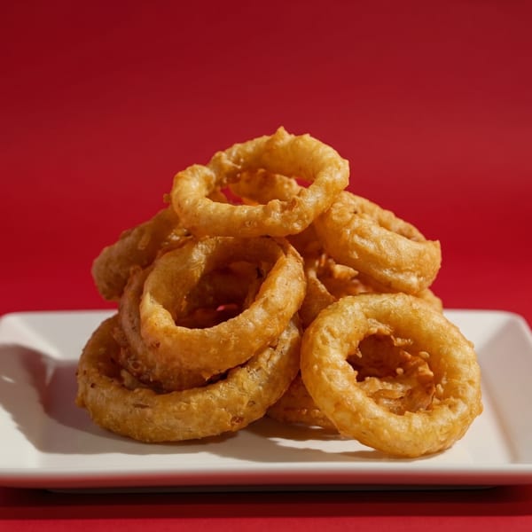 A pile of golden-brown onion rings on a white rectangular plate against a vibrant red background.