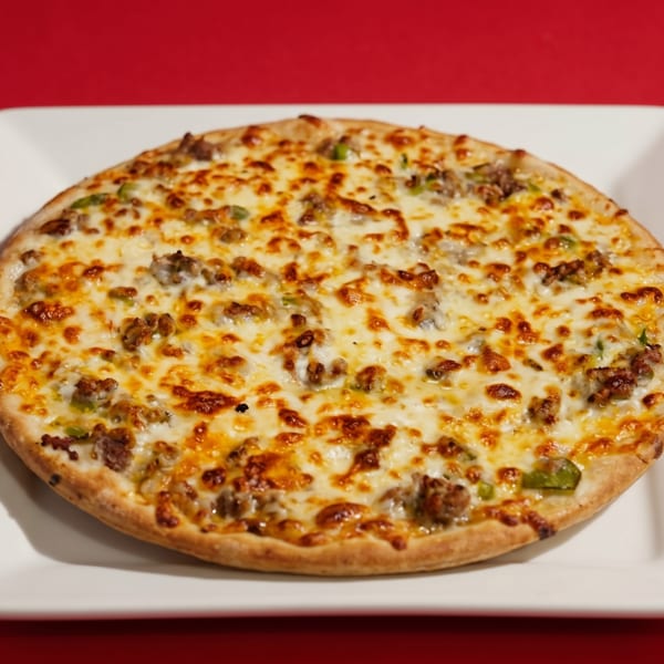 A whole round pizza with melted cheese, sausage, and green peppers on a white square plate.