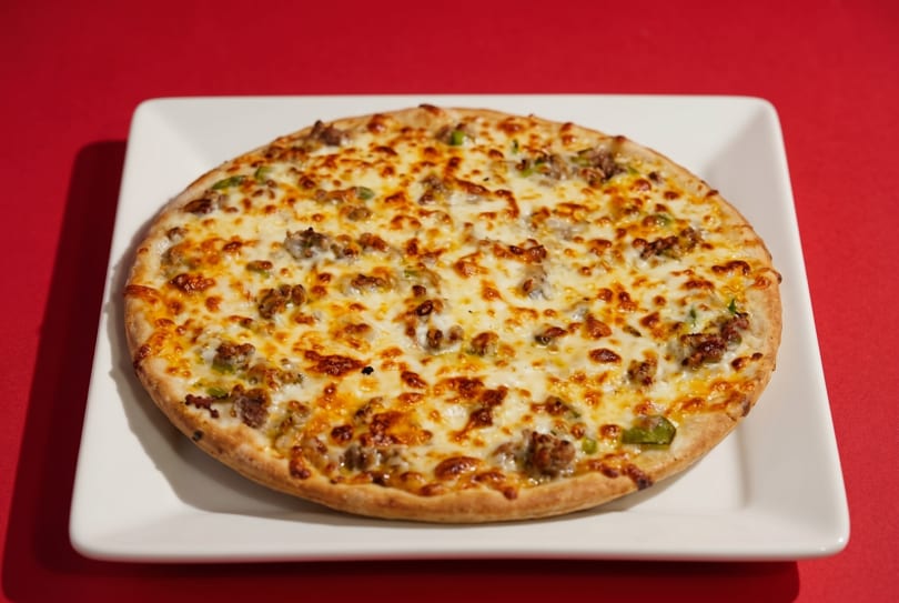 A whole round pizza with melted cheese, sausage, and green peppers on a white square plate.
