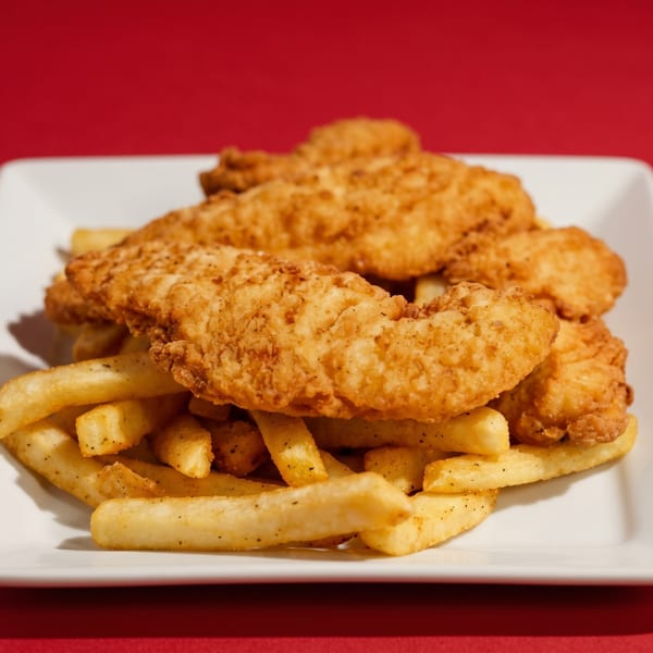 Crispy golden chicken tenders and seasoned french fries on a white rectangular plate against a red background.