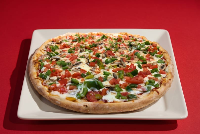 A whole vegetarian pizza with mushrooms, green peppers, and tomatoes on a white plate.
