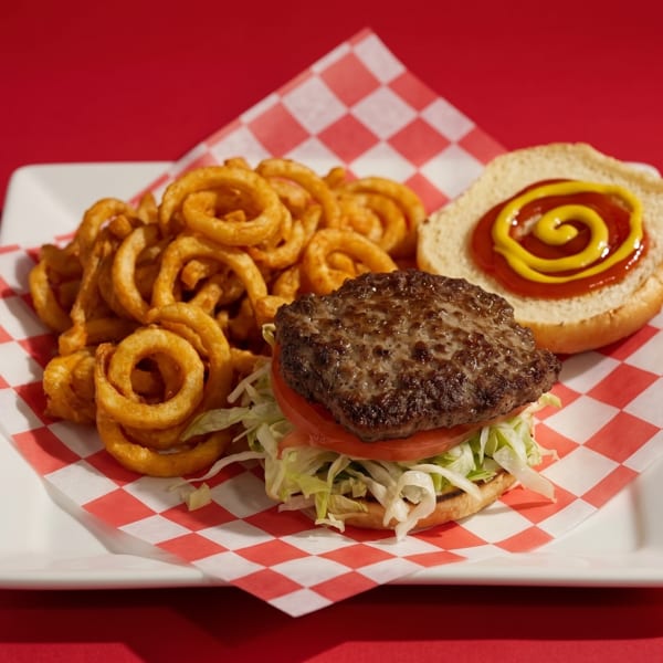 A hamburger with lettuce, tomato, and a side of curly fries on a red and white checkered paper.